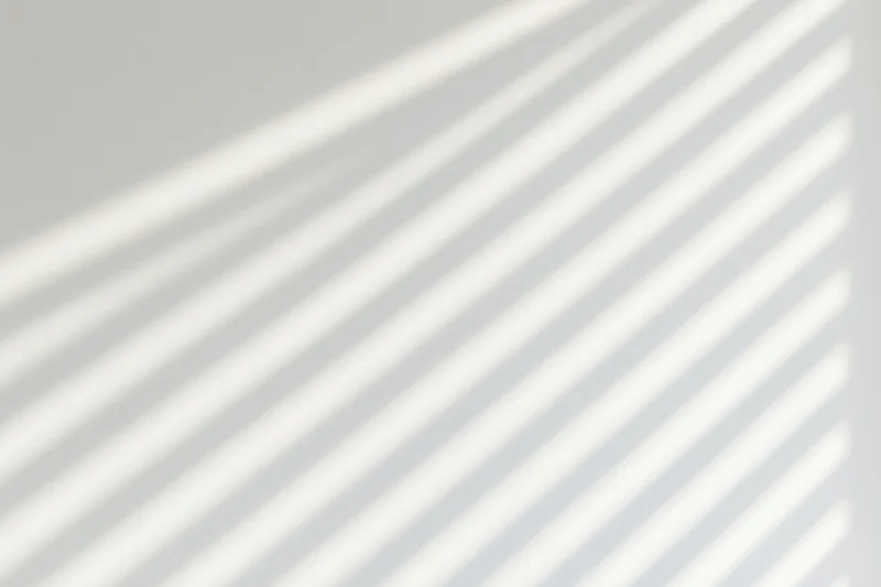 Diagonal light and shadow stripes from a window on a white wall