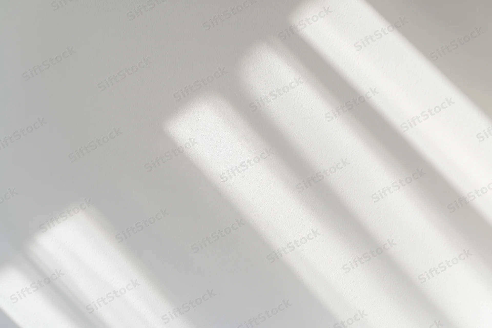 Diagonal light streaks from a window casting soft shadows on a white wall