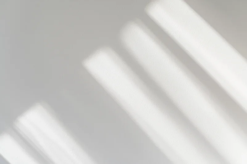 Diagonal light streaks from a window casting soft shadows on a white wall