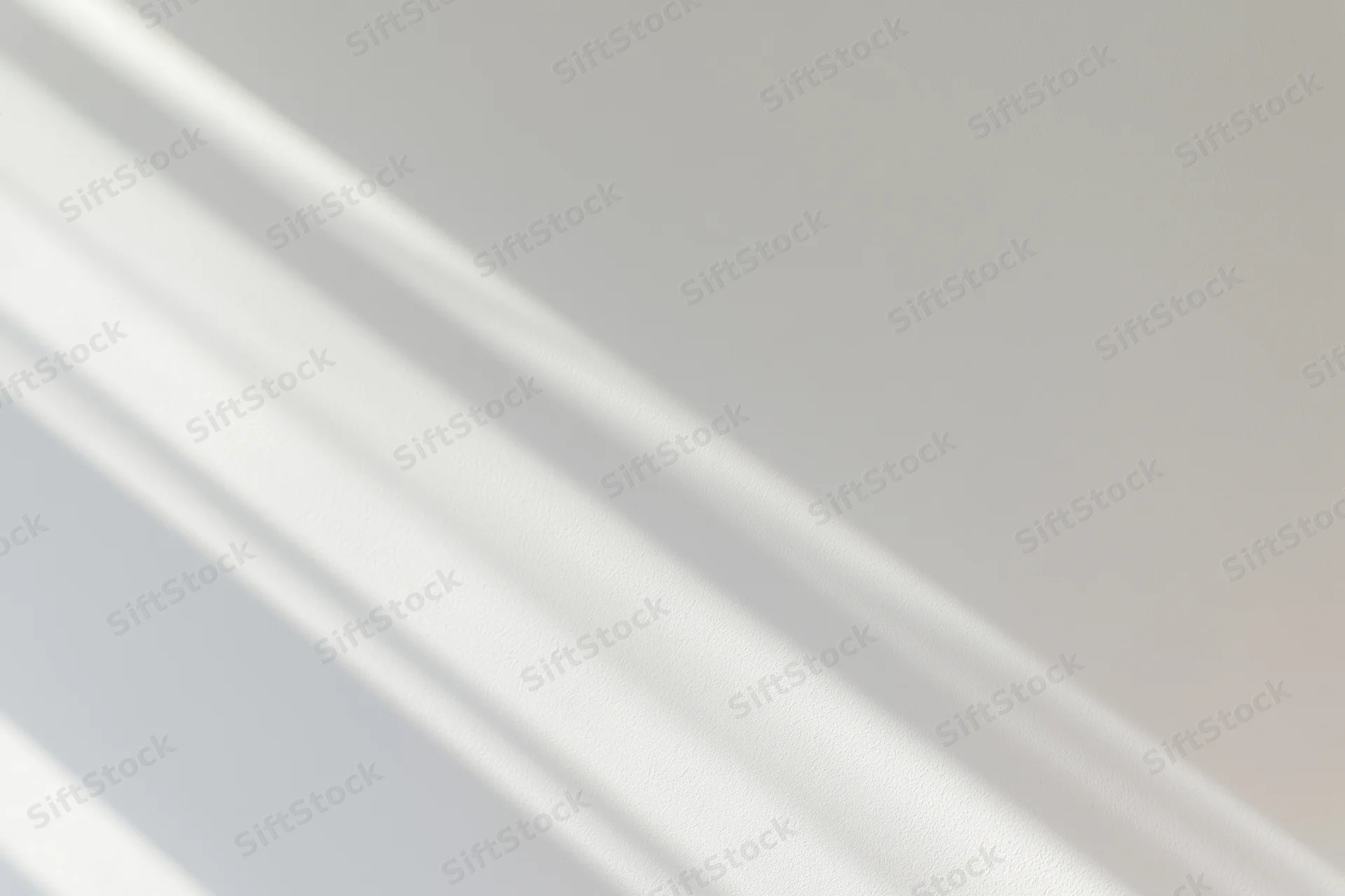 Diagonal window light casting soft overlapping shadow streaks on a neutral indoor surface