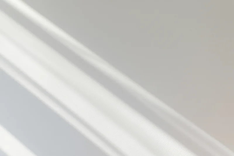 Diagonal window light casting soft overlapping shadow streaks on a neutral indoor surface