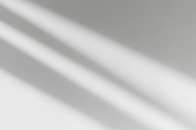 Diagonal window light casting soft overlapping shadow streaks across a plain surface