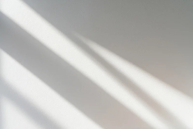 Diagonal light beams casting soft overlapping shadows on a white wall