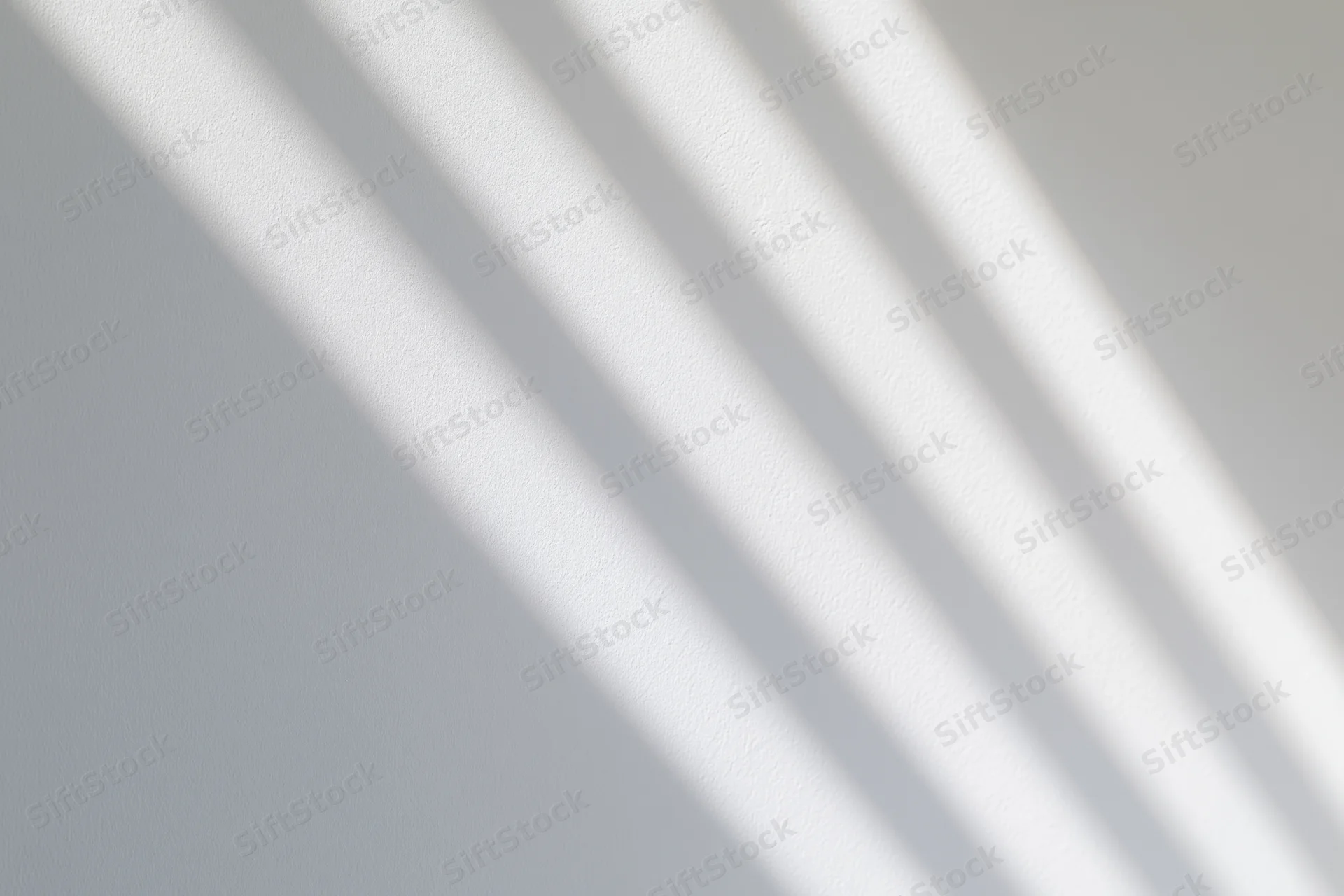 Diagonal bands of soft sunlight and shadow on a white wall