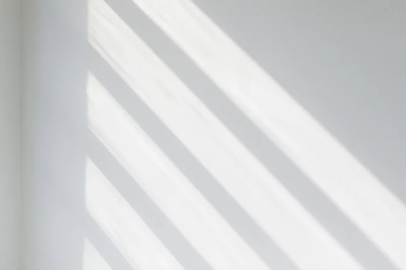 Diagonal light bands cast by window blinds on a white wall interior