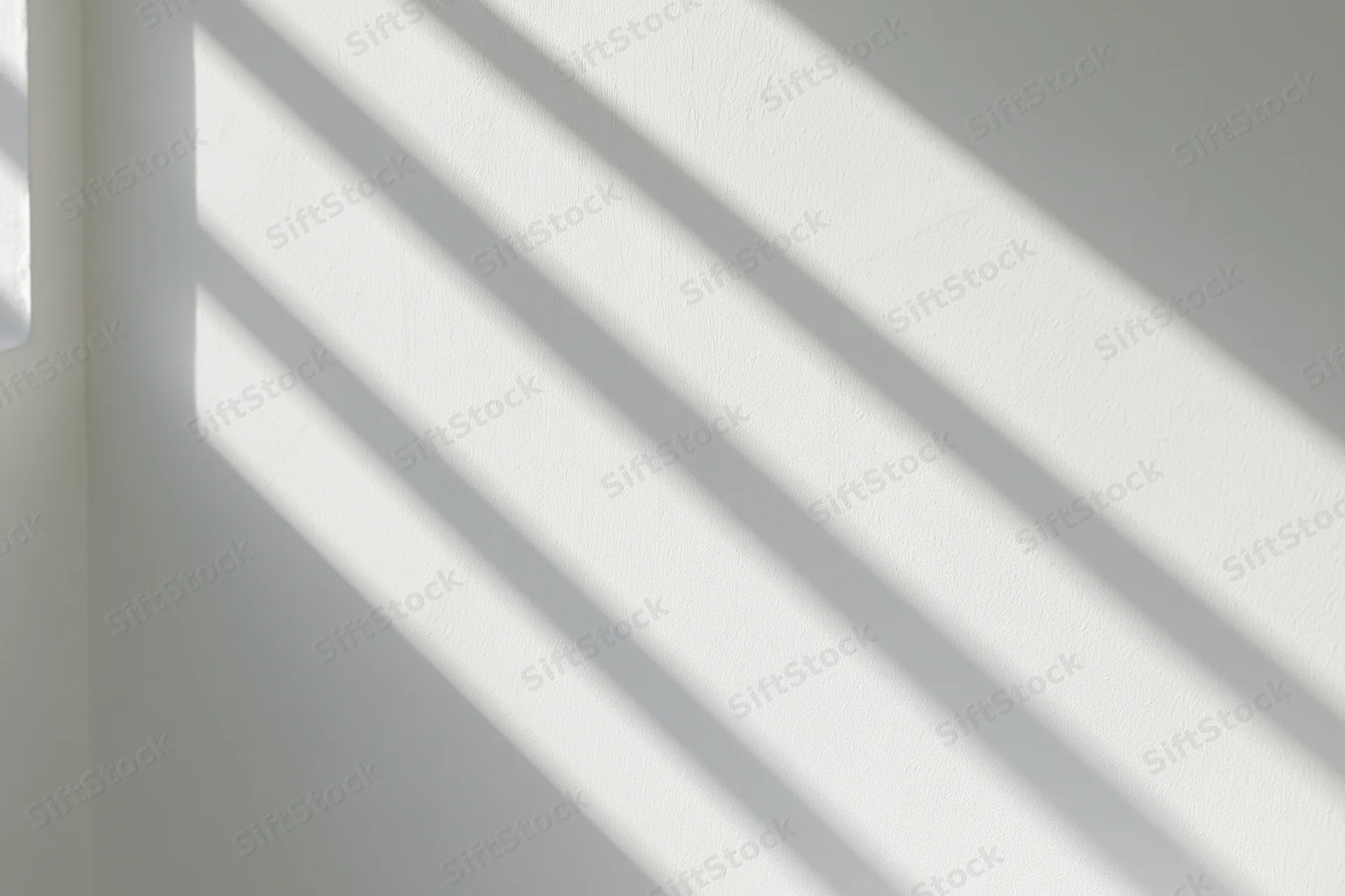 Diagonal sunlight casting parallel shadows across a white interior wall