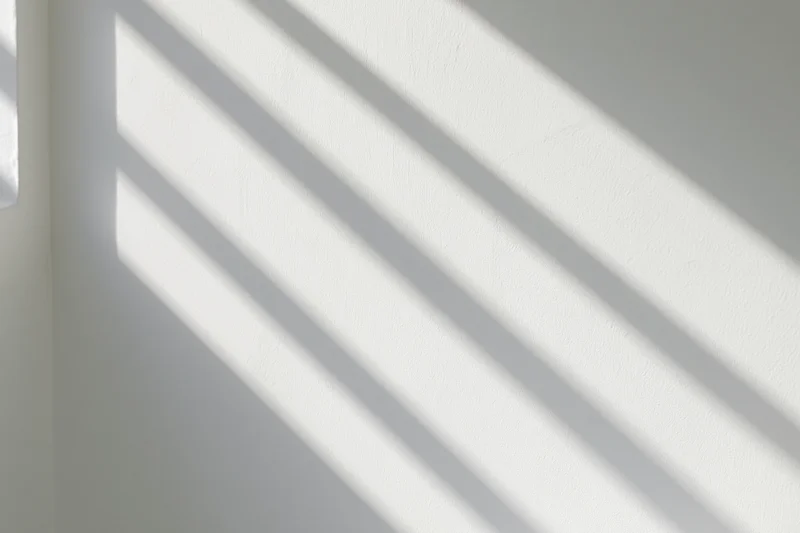 Diagonal sunlight casting parallel shadows across a white interior wall