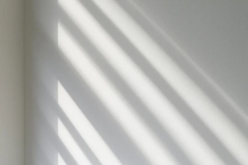 Diagonal light bands cast by window blinds on a white interior wall