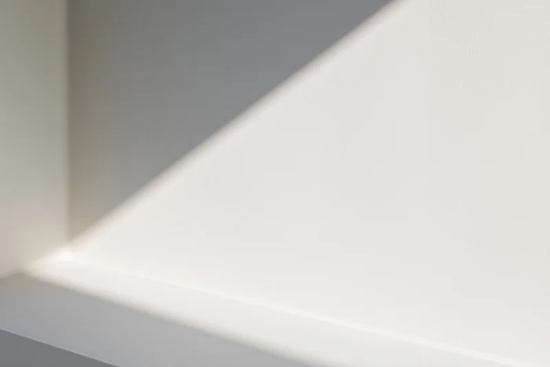 Diagonal beam of natural light casting soft shadow across white interior wall corner