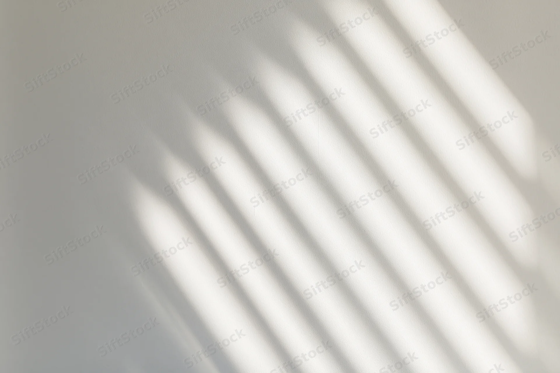 Diagonal light stripes from a window casting soft shadows on a white wall indoors