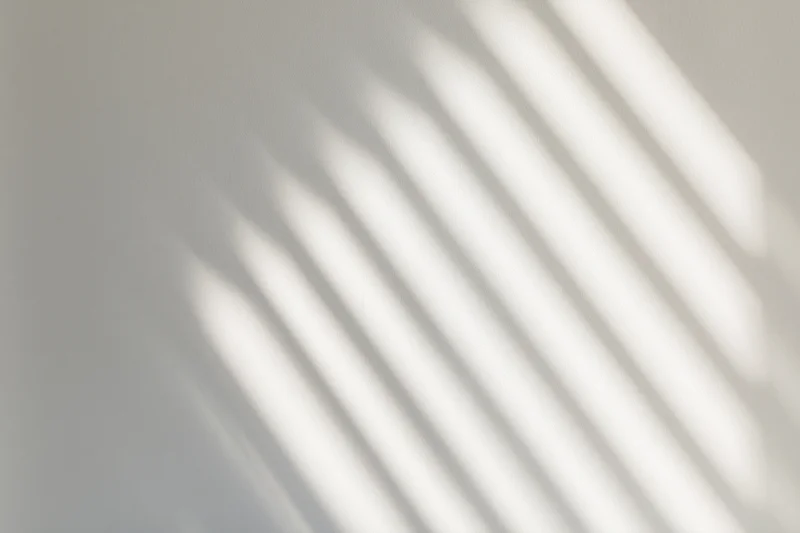 Diagonal light stripes from a window casting soft shadows on a white wall indoors