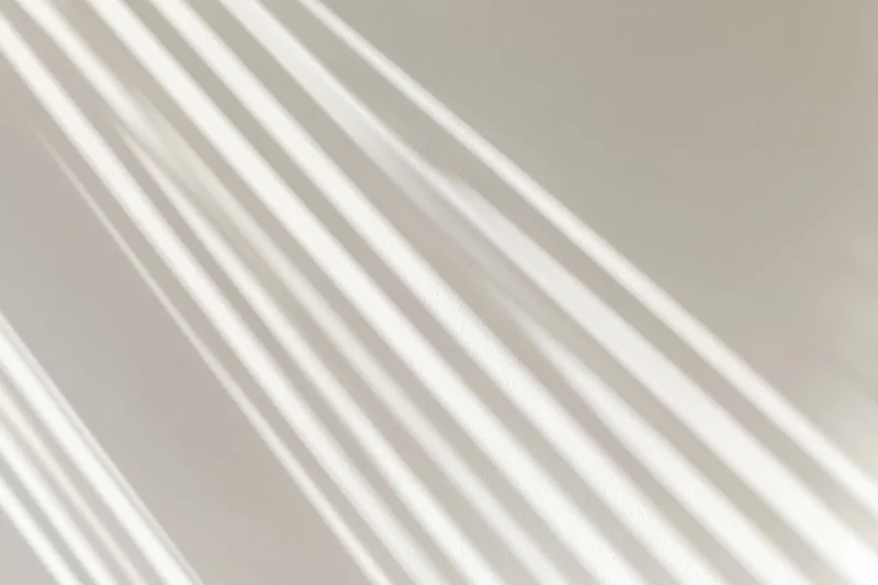 Diagonal light stripes casting soft shadows on a neutral wall indoors