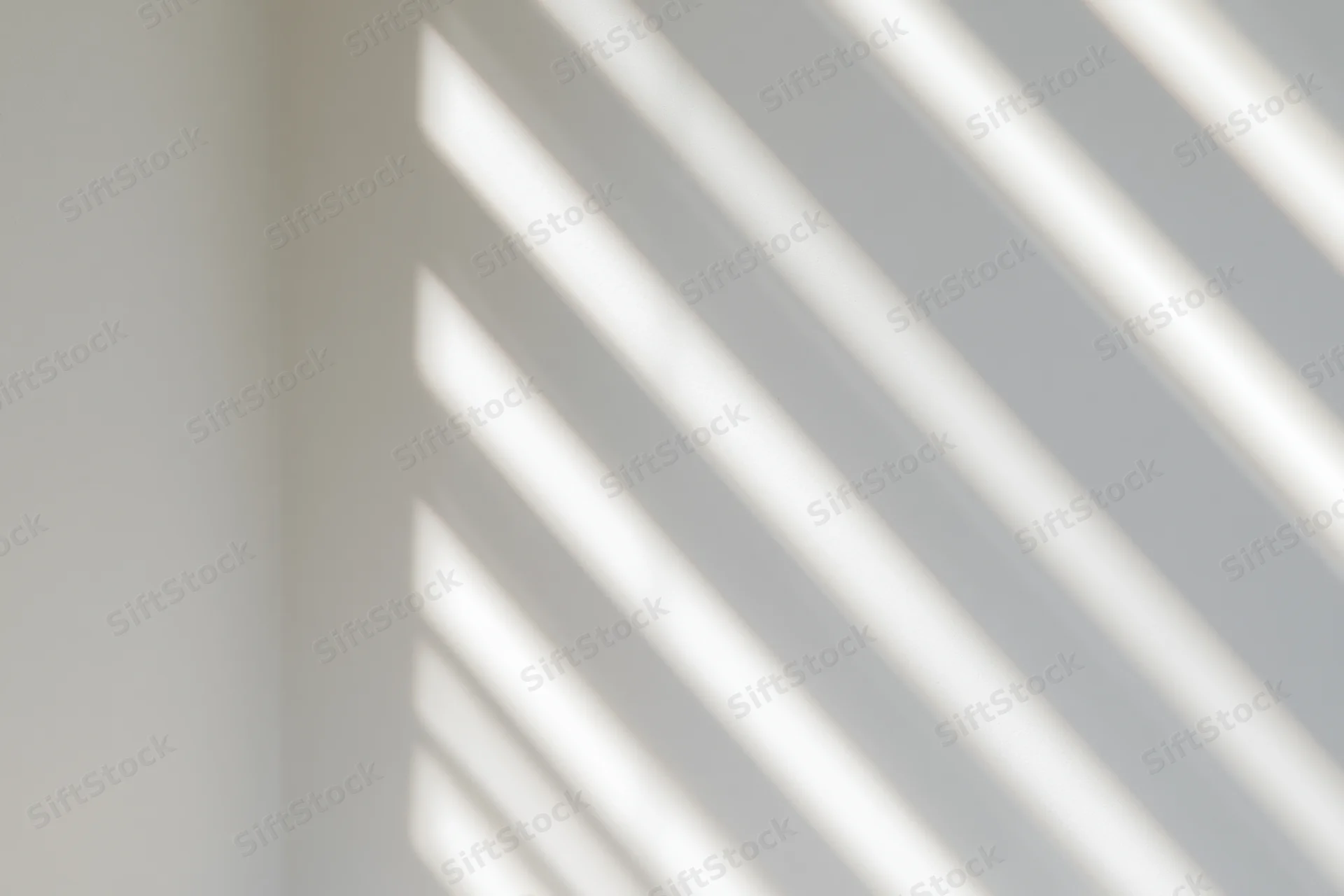 Diagonal light stripes from window blinds cast soft shadows on a white interior wall