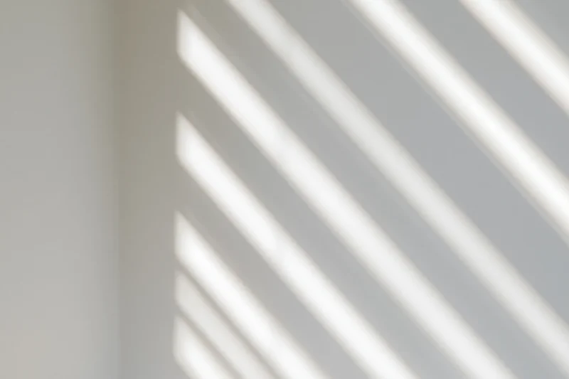 Diagonal light stripes from window blinds cast soft shadows on a white interior wall