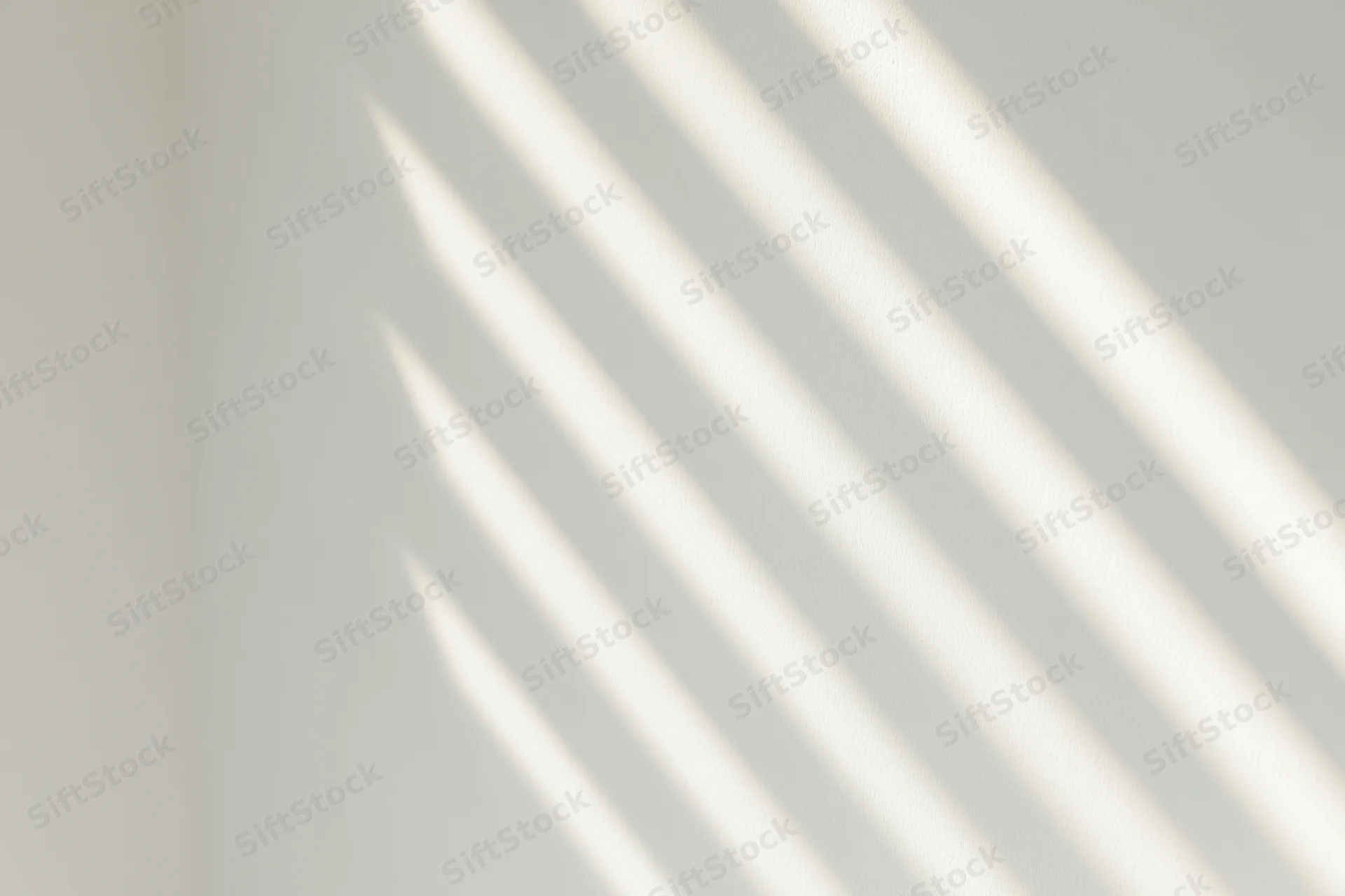 Diagonal light stripes cast by window blinds on a white interior wall