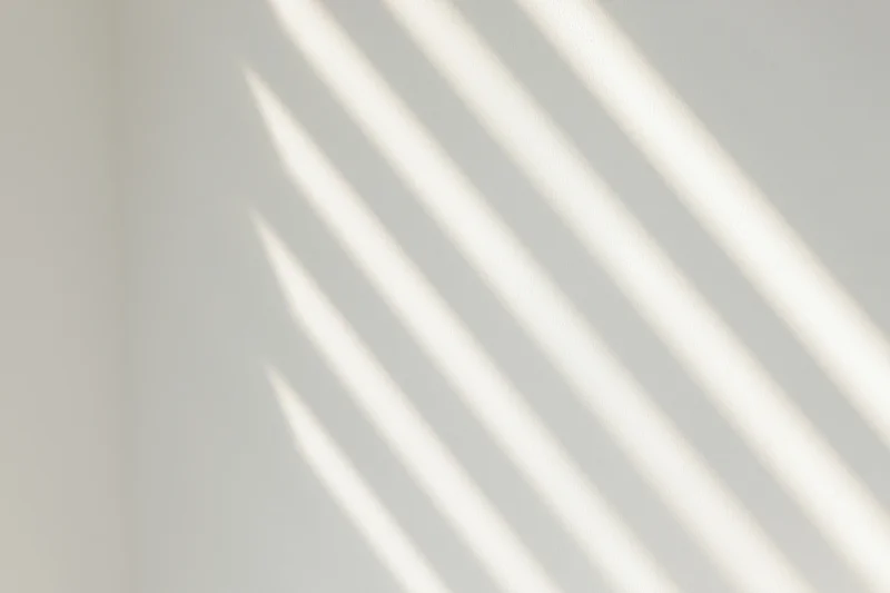 Diagonal light stripes cast by window blinds on a white interior wall