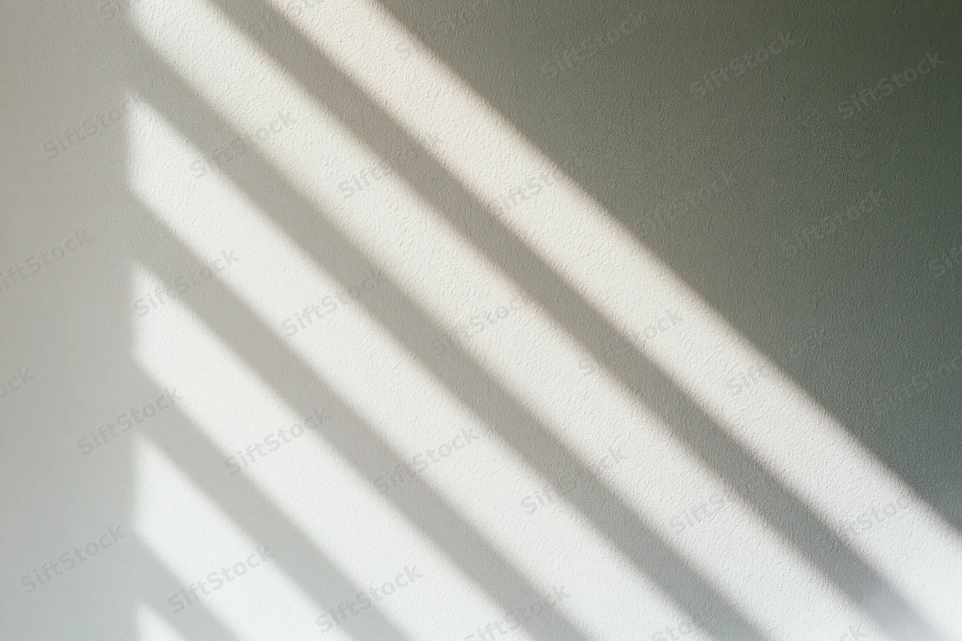 Diagonal shadows from window blinds cast across a plain off-white wall in soft natural light