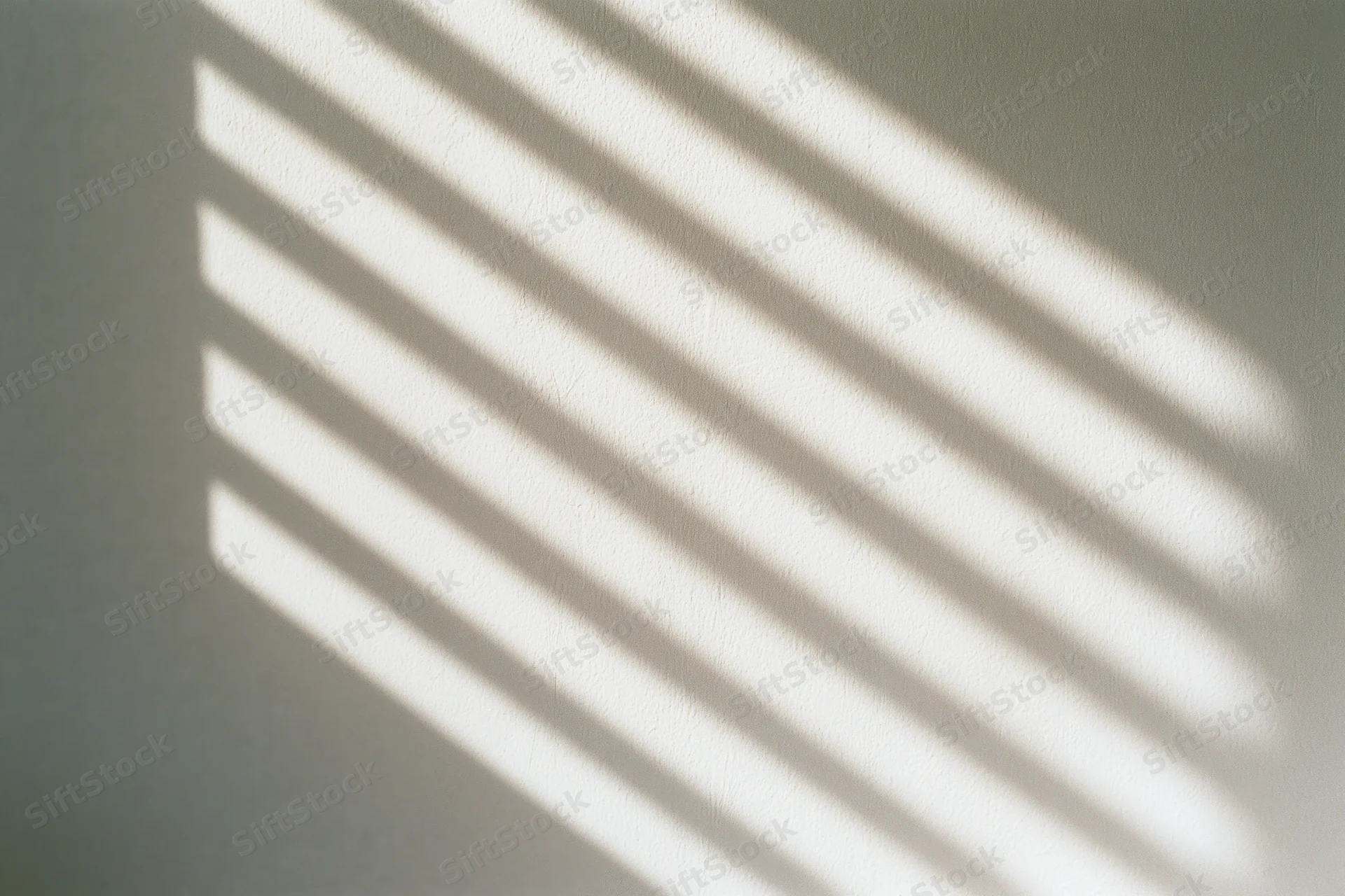 Diagonal shadow pattern from window blinds on off-white wall