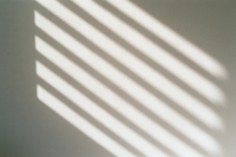 Diagonal shadow pattern from window blinds on off-white wall