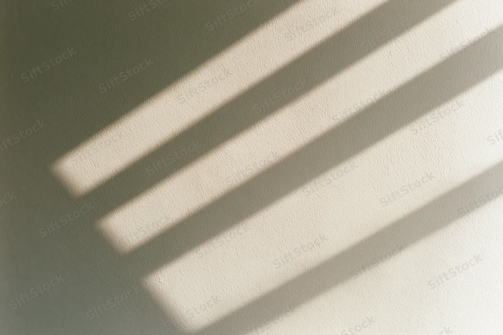 Diagonal shadows from window blinds cast across a plain off-white wall in soft natural light