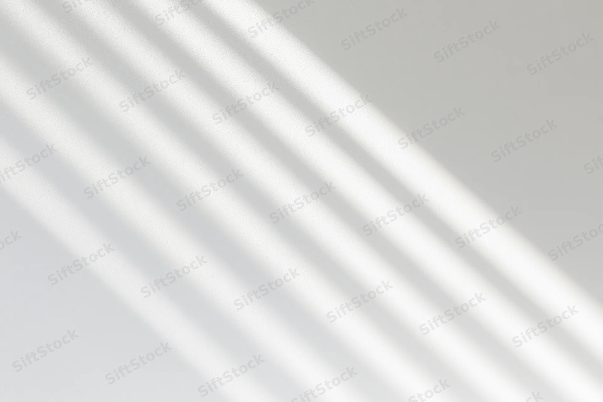 Diagonal shadow lines from window blinds on a white wall
