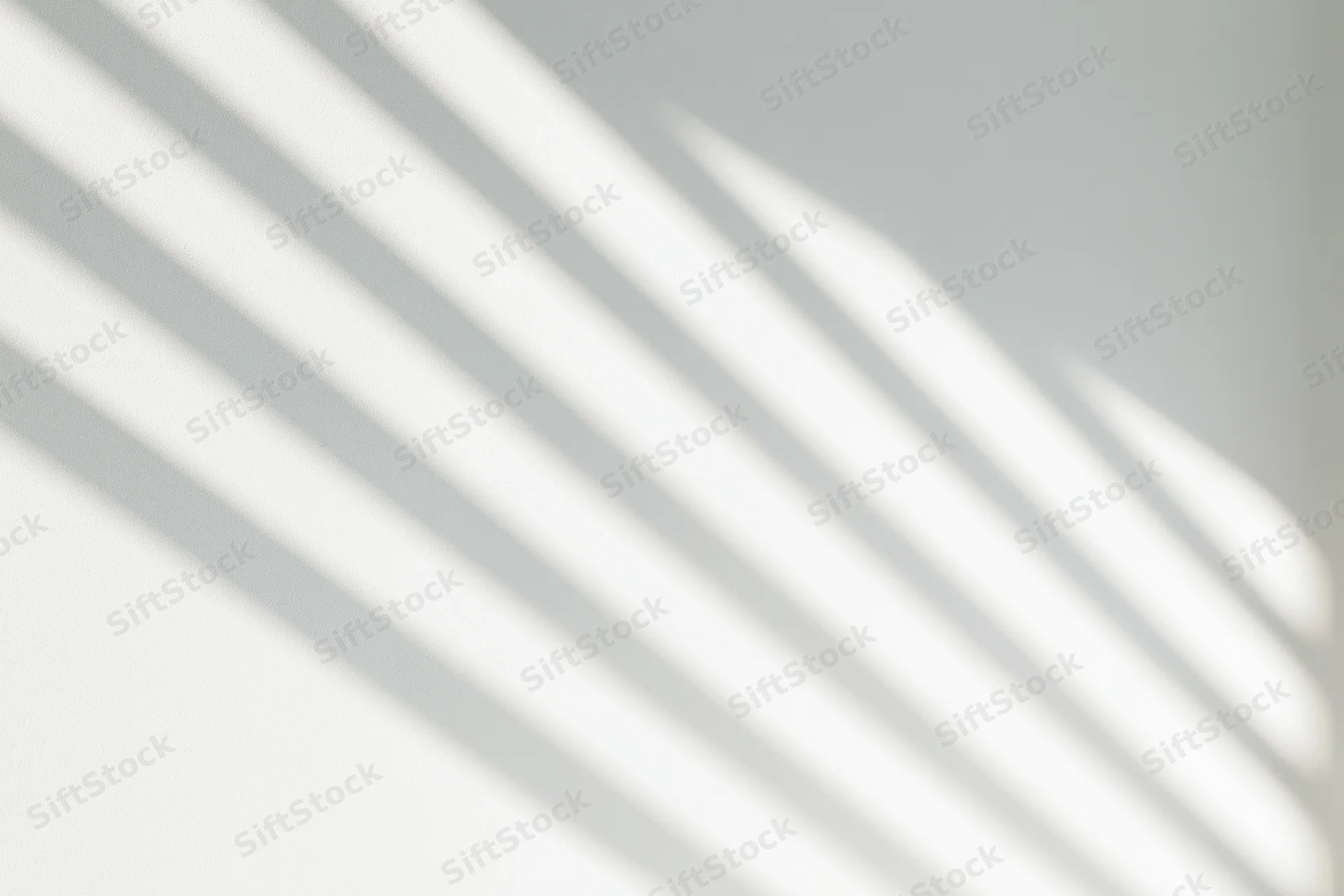Diagonal shadow lines from a window cast across a plain white wall in soft natural light