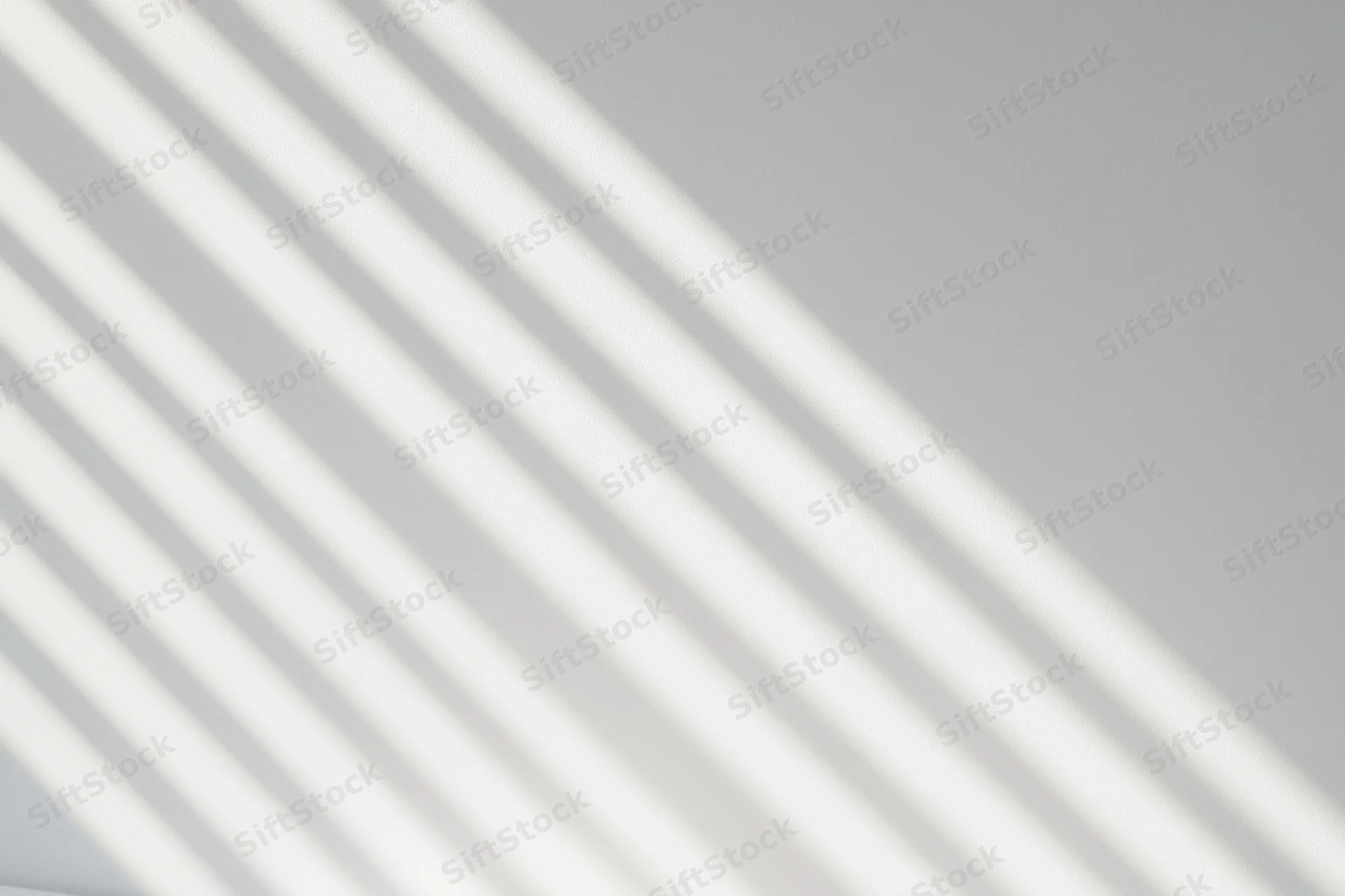 Diagonal shadow stripes from window blinds on a white wall interior