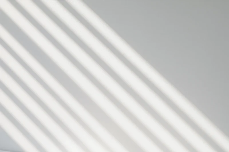 Diagonal shadow stripes from window blinds on a white wall interior