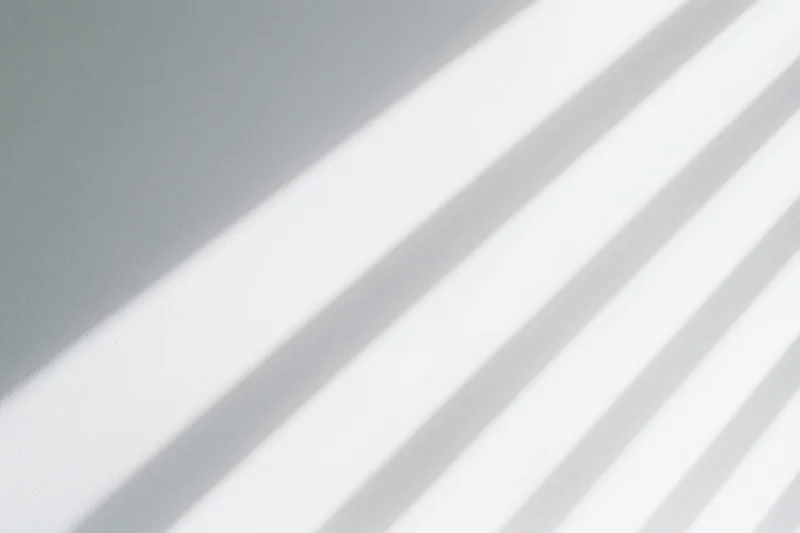 Diagonal light and shadow stripes across a plain white interior wall