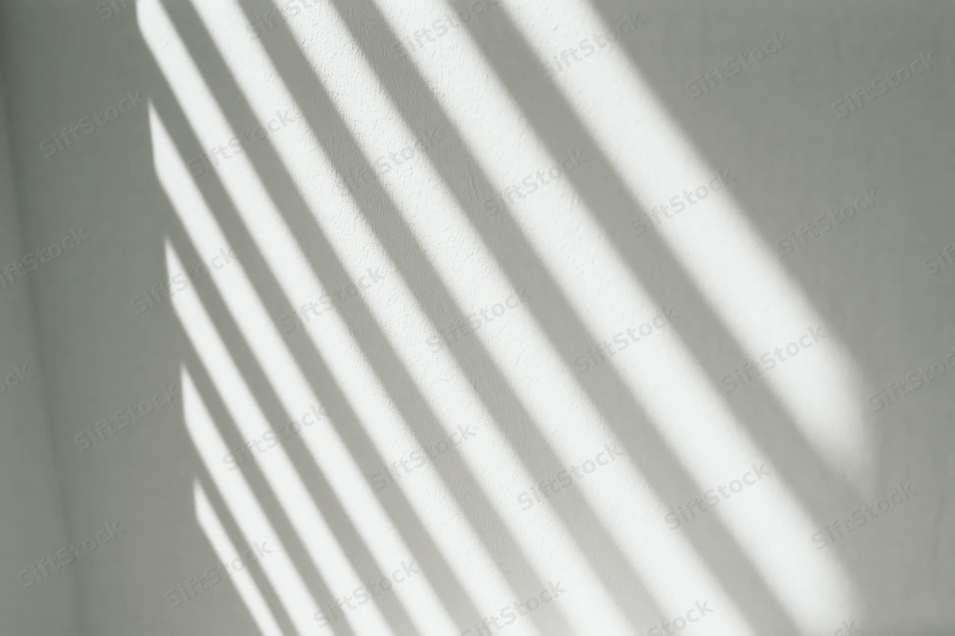 Diagonal light stripes from window blinds cast across a white interior wall