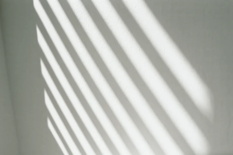 Diagonal light stripes from window blinds cast across a white interior wall
