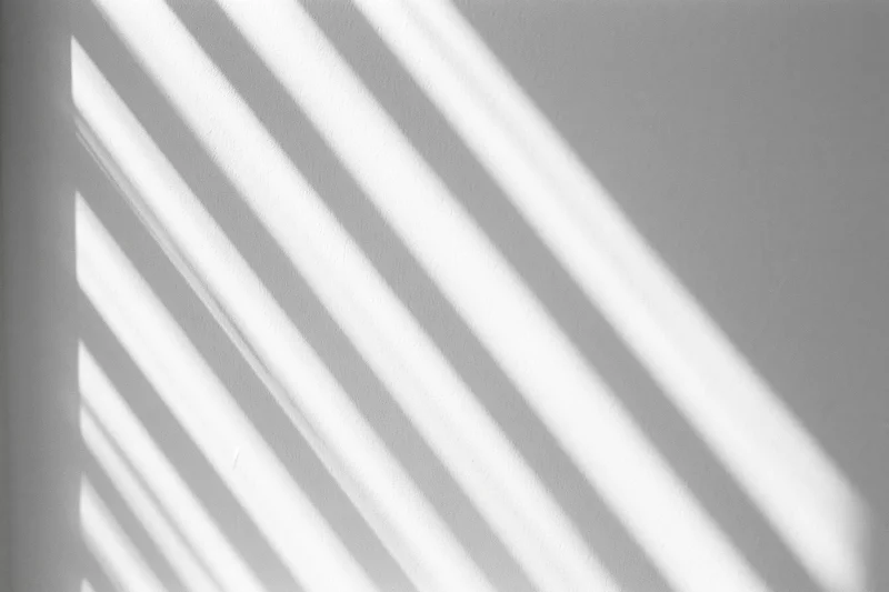 Diagonal light and shadow stripes cast across a plain white interior wall