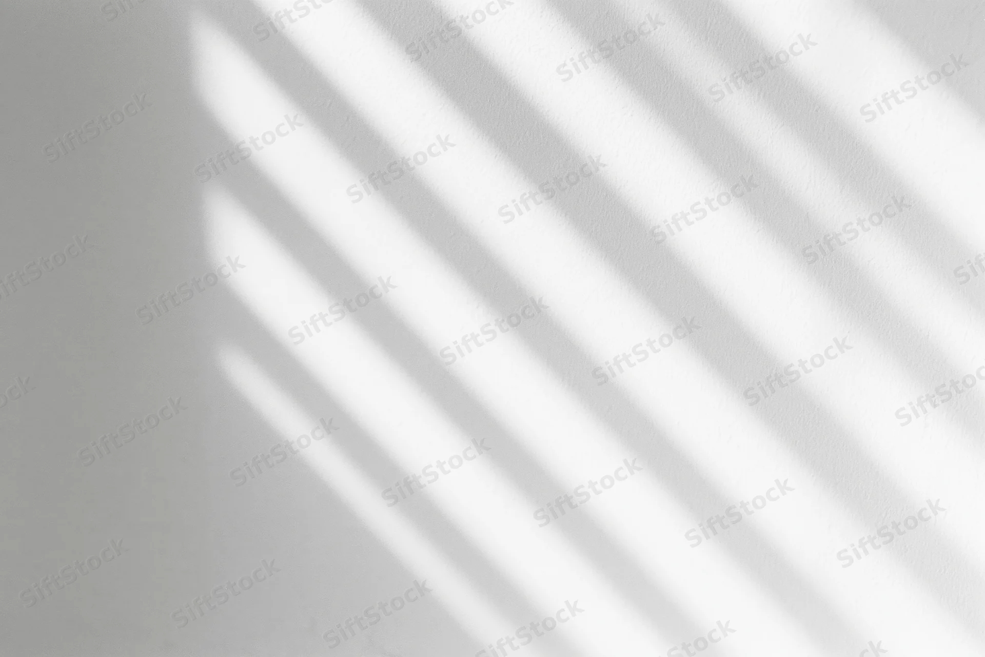 Diagonal light and shadow stripes cast across a plain white interior wall
