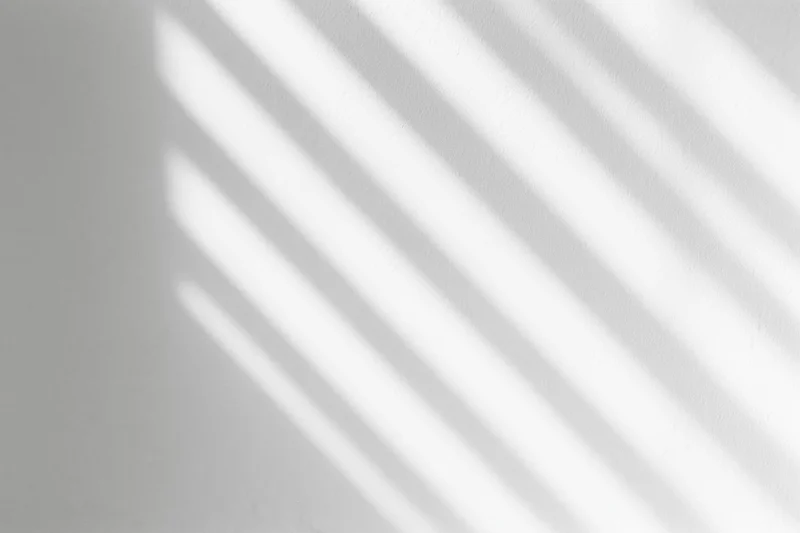 Diagonal light and shadow stripes cast across a plain white interior wall