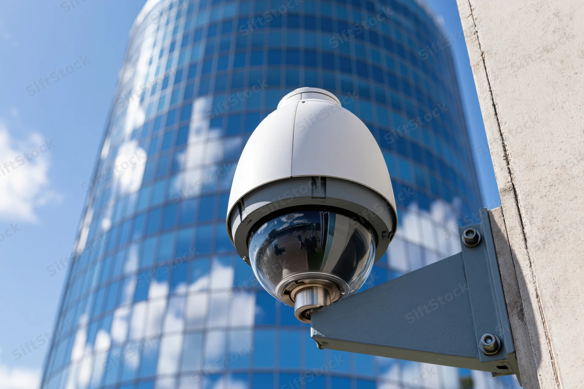 Dome security camera mounted on metal bracket against glass skyscraper exterior