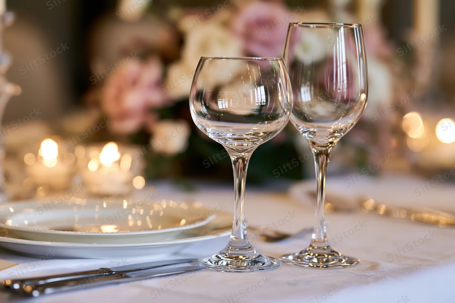 Two empty crystal wine glasses on a formally set dinner table with floral centerpiece and candles