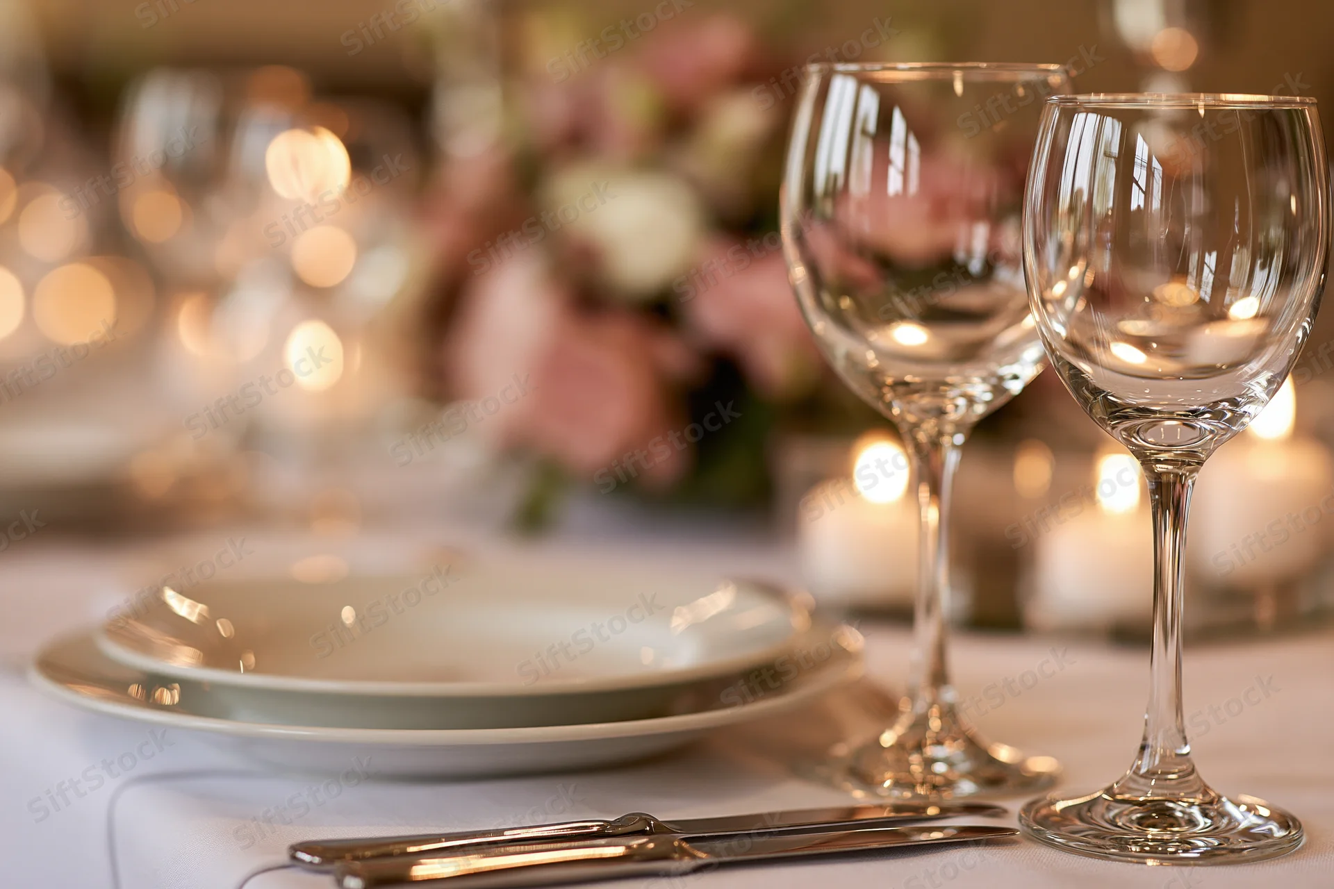 Elegant dinner table set with crystal wine glasses and fine dining ware under soft candlelight