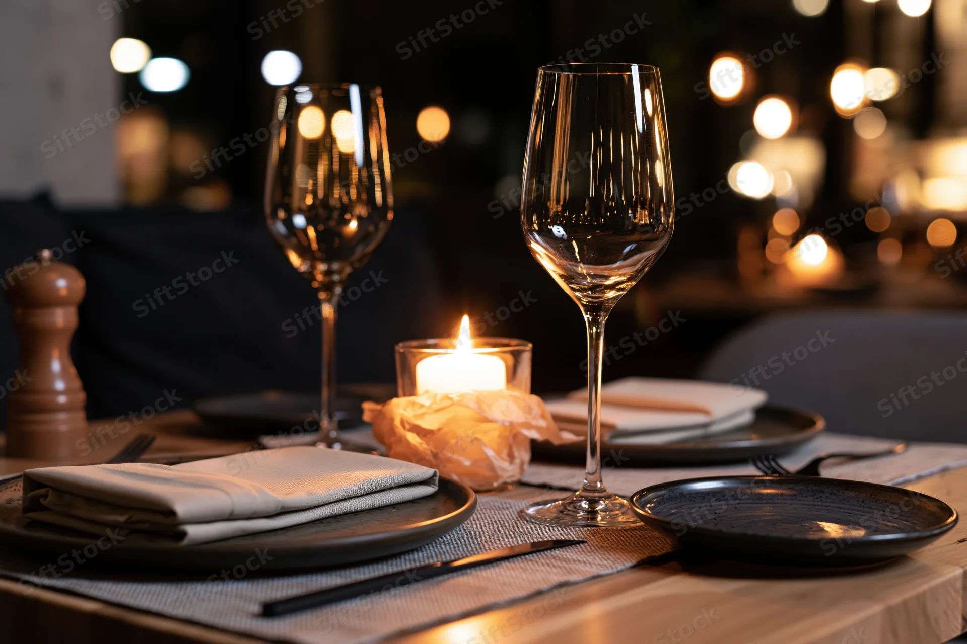 Elegant restaurant table set for two with wine glasses, plates, and candlelight on wooden surface