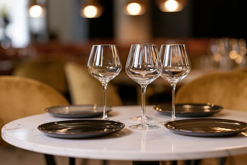 Four empty wine glasses arranged on a marble table with black plates in a restaurant dining area