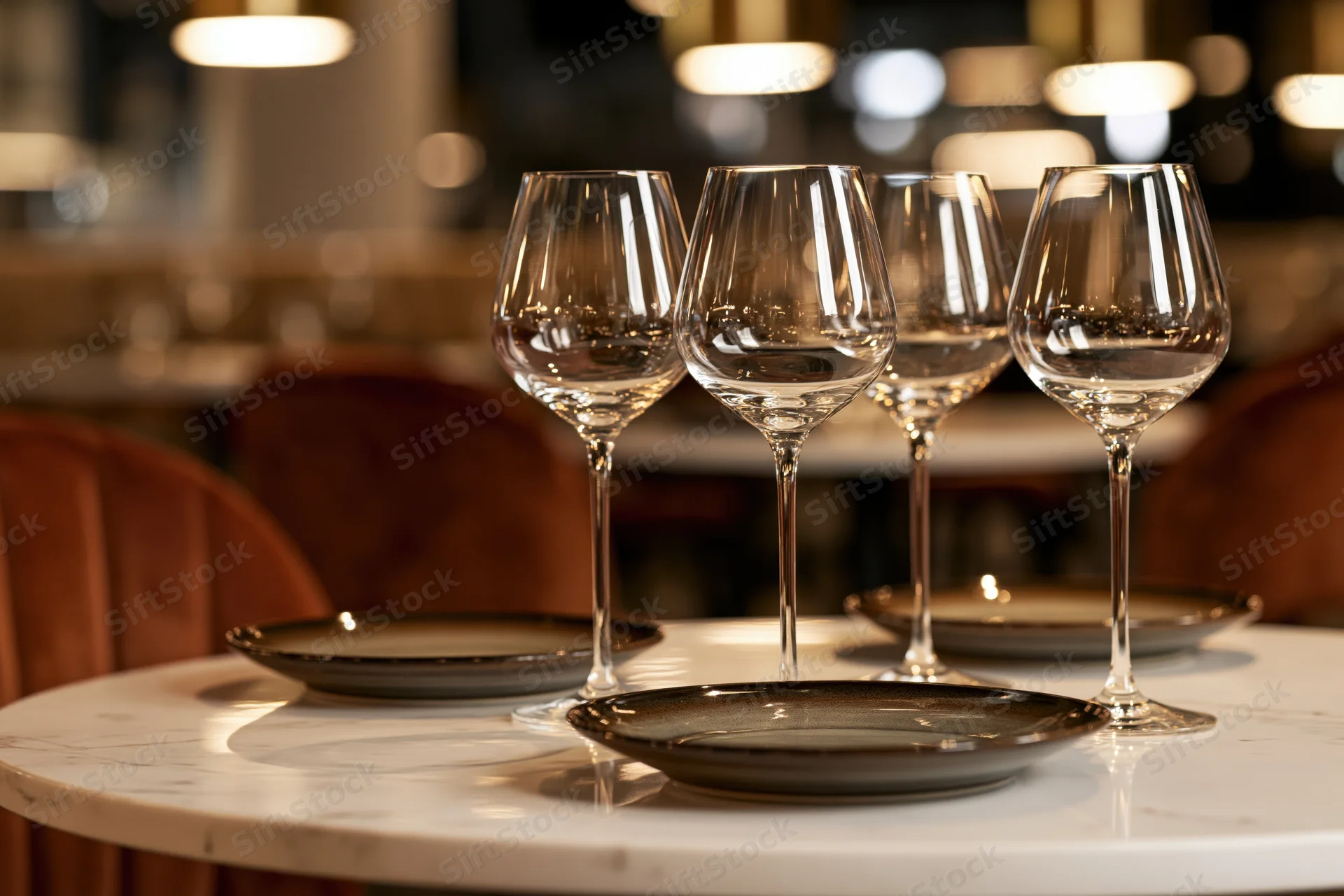 Four empty wine glasses arranged on a marble table with plates in a restaurant dining area