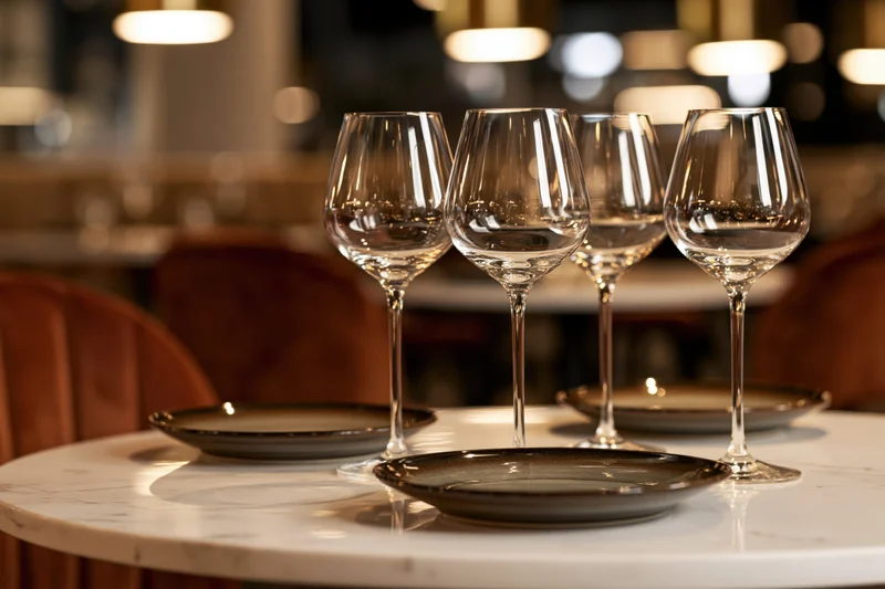 Four empty wine glasses arranged on a marble table with plates in a restaurant dining area