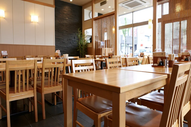 Empty wooden tables and chairs arranged in a casual japanese restaurant dining room