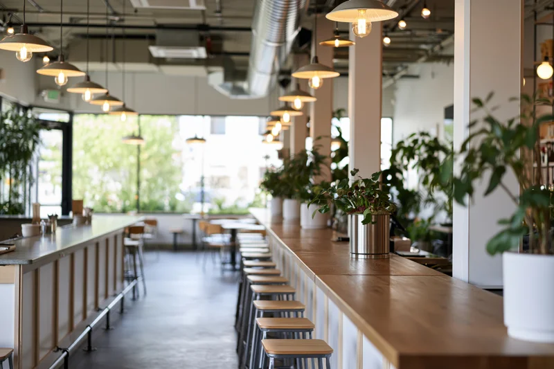 Long view down empty cafe counter with pendant lights and potted plants along the bar