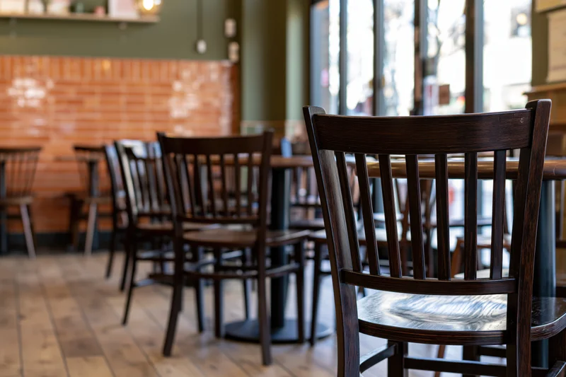Empty cafe interior with dark wooden chairs and round tables arranged along brick wall and windows