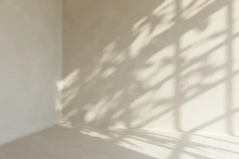 Empty cream-white corner room with sunlight casting window shadow on walls and floor