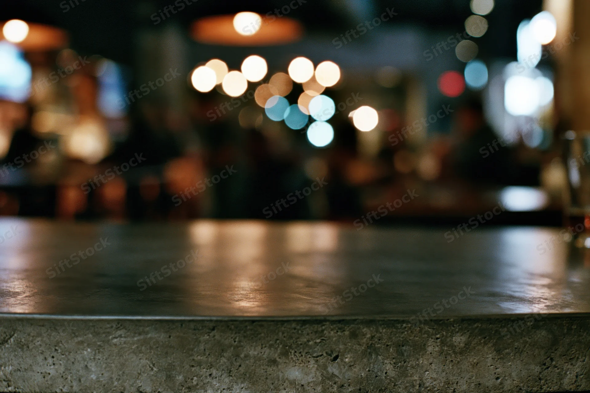 Dark concrete bar countertop in sharp focus with blurred lights in background