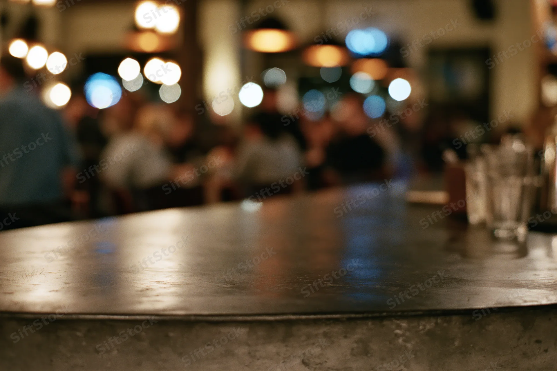 Dark concrete bar countertop in sharp focus with blurred people and lights in background