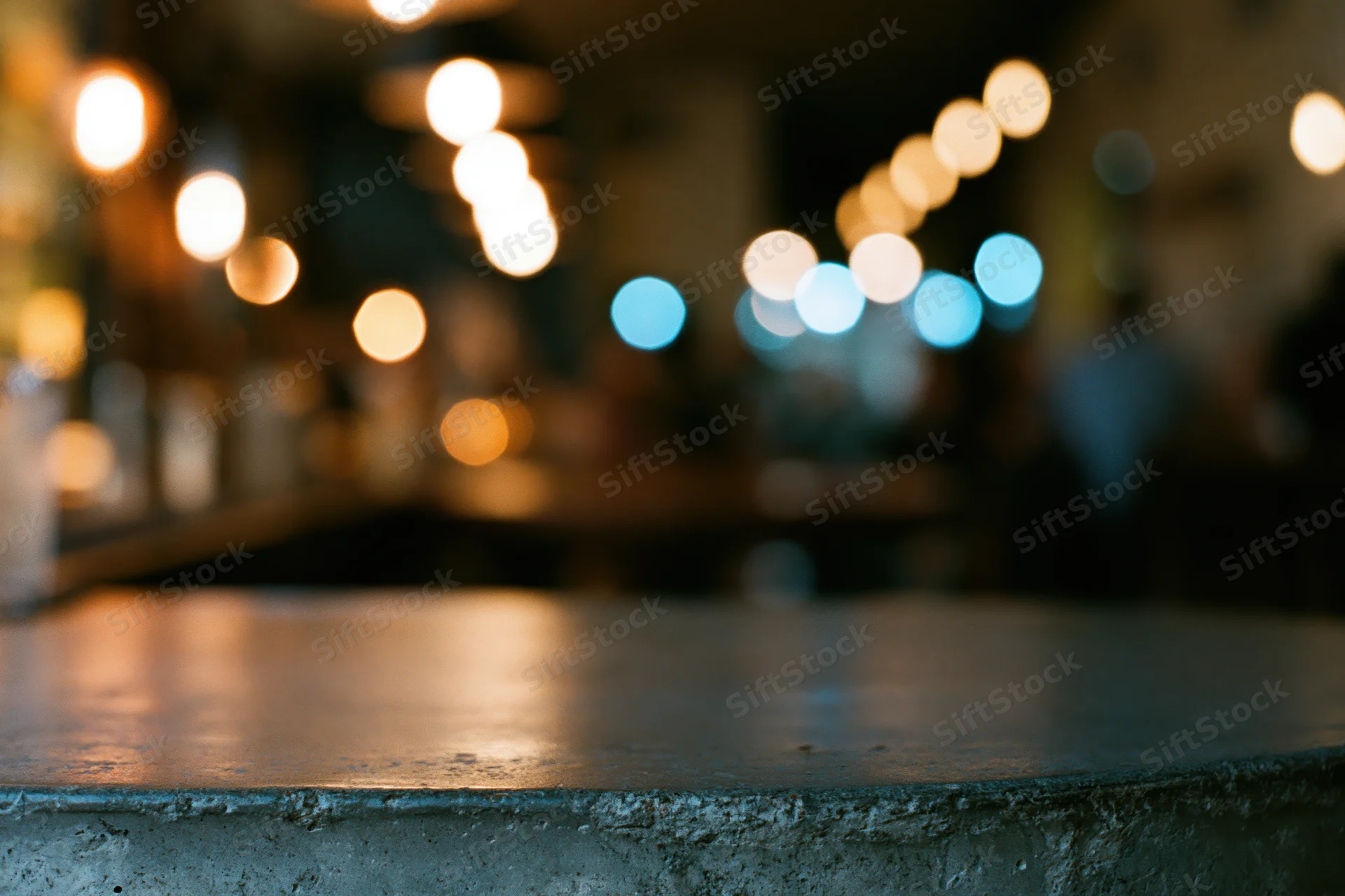Dark concrete table surface in sharp focus with blurred lights in background