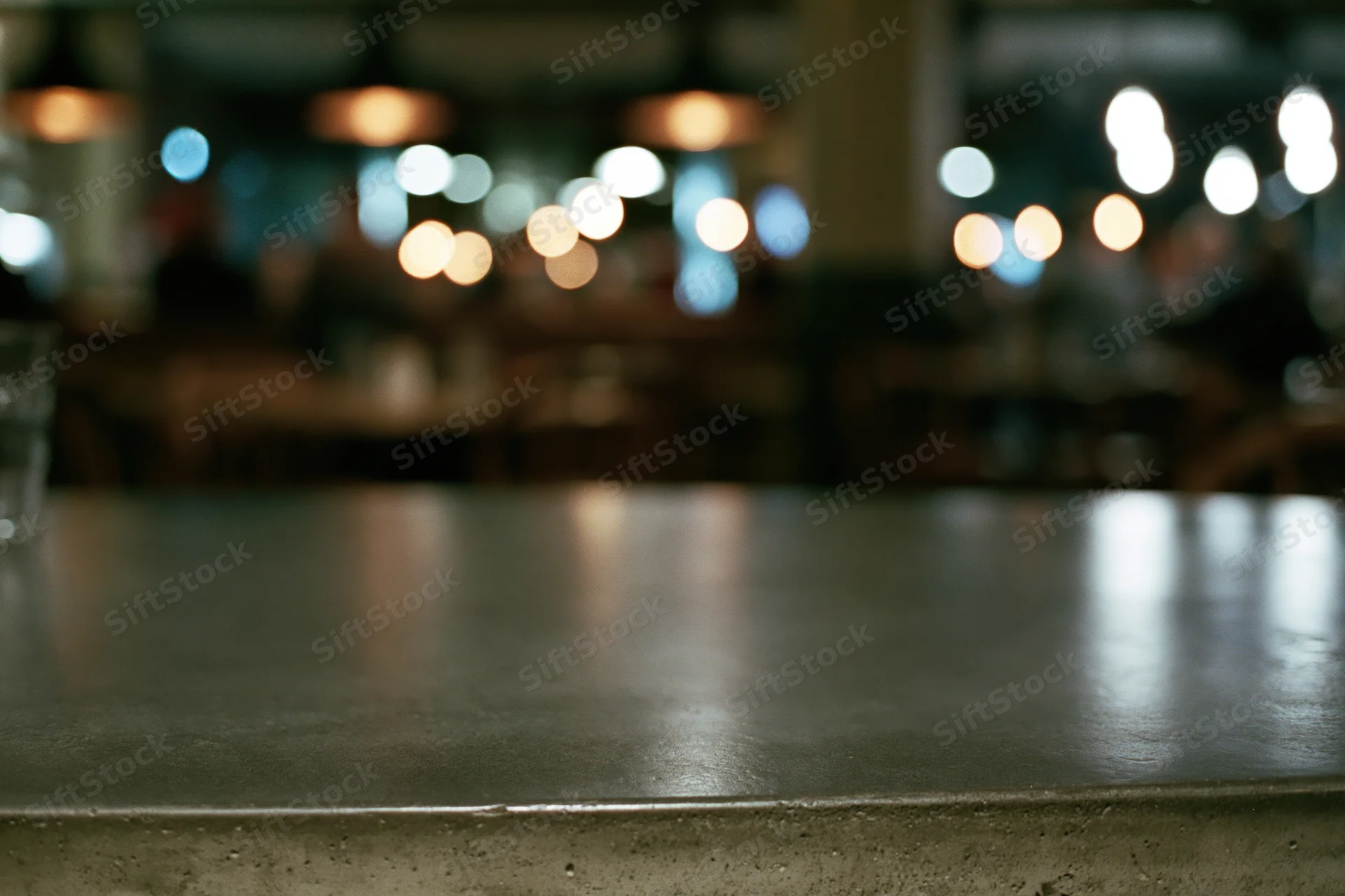 Empty concrete table surface in sharp focus with blurred restaurant interior and bokeh lights in background
