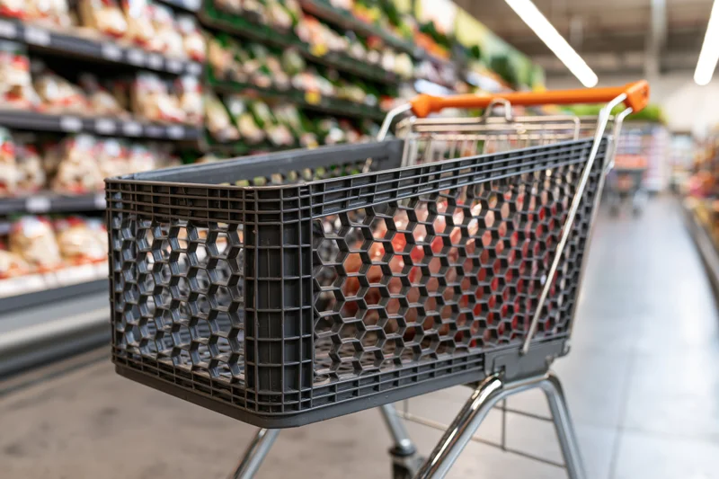 Empty dark grey plastic shopping cart with orange handle in a supermarket aisle